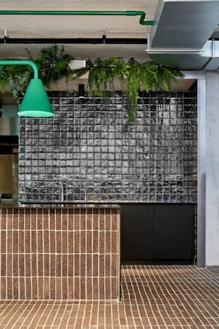 Groen van kabelboom en planten en grafisch zwart ontmoeten elkaar in de open keuken van het restaurant. Hier bedienen de werknemers zichzelf, zodat alle ruimtes vrij toegankelijk en laagdrempelig zijn. fotografie Philip Jintes @ Phenster