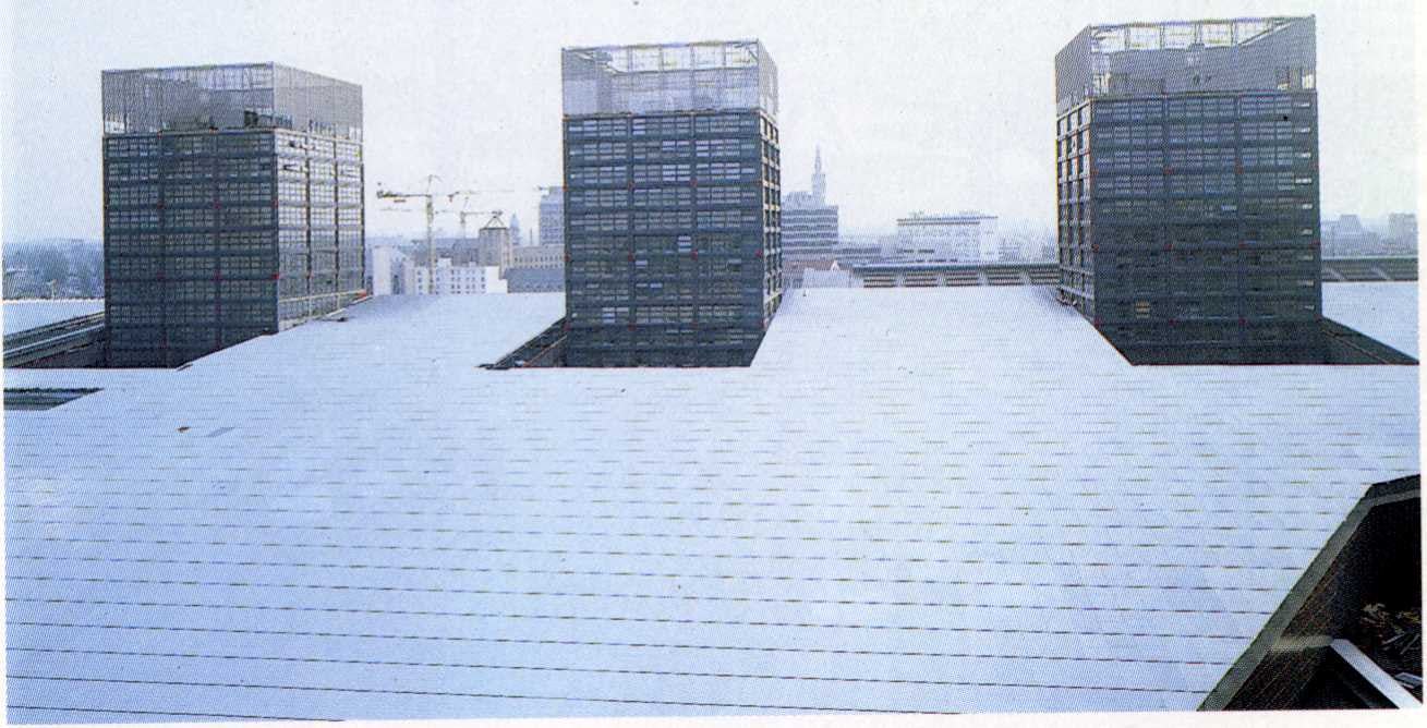 De drie kantoortorentjes steken door het aluminiumrooster beklede dak van het winkelcentrum heen - Beeld Philippe Ruault

