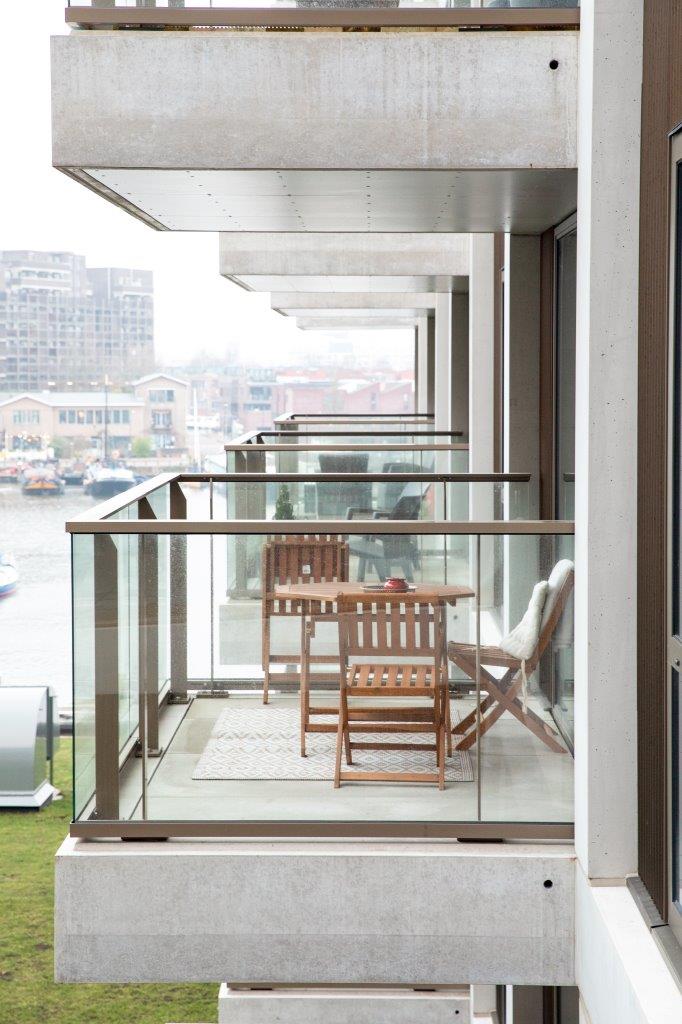 Over de oude wijnterminal kragen eenzijdig georiënteerde woningen vijf meter uit. Hun half-inpandige balkons kijken uit over de haven en het nieuwe groene dak van de terminal. Beeld Thijs van Stigt