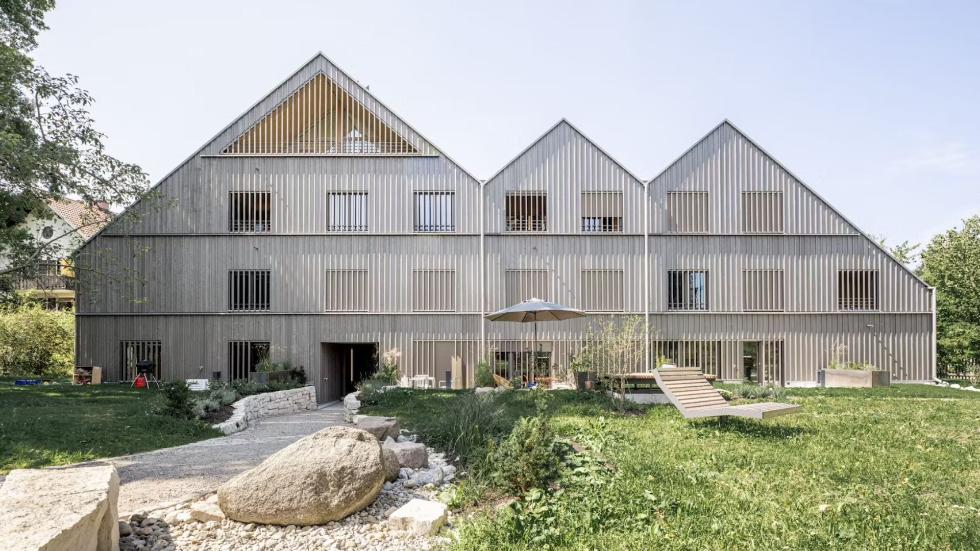 Neue Derzbachhof in München, gezien vanaf de ruime fruitweide met speelplekken, ligstoelen en verhoogde bedden. Beeld Thomas Weinbergen