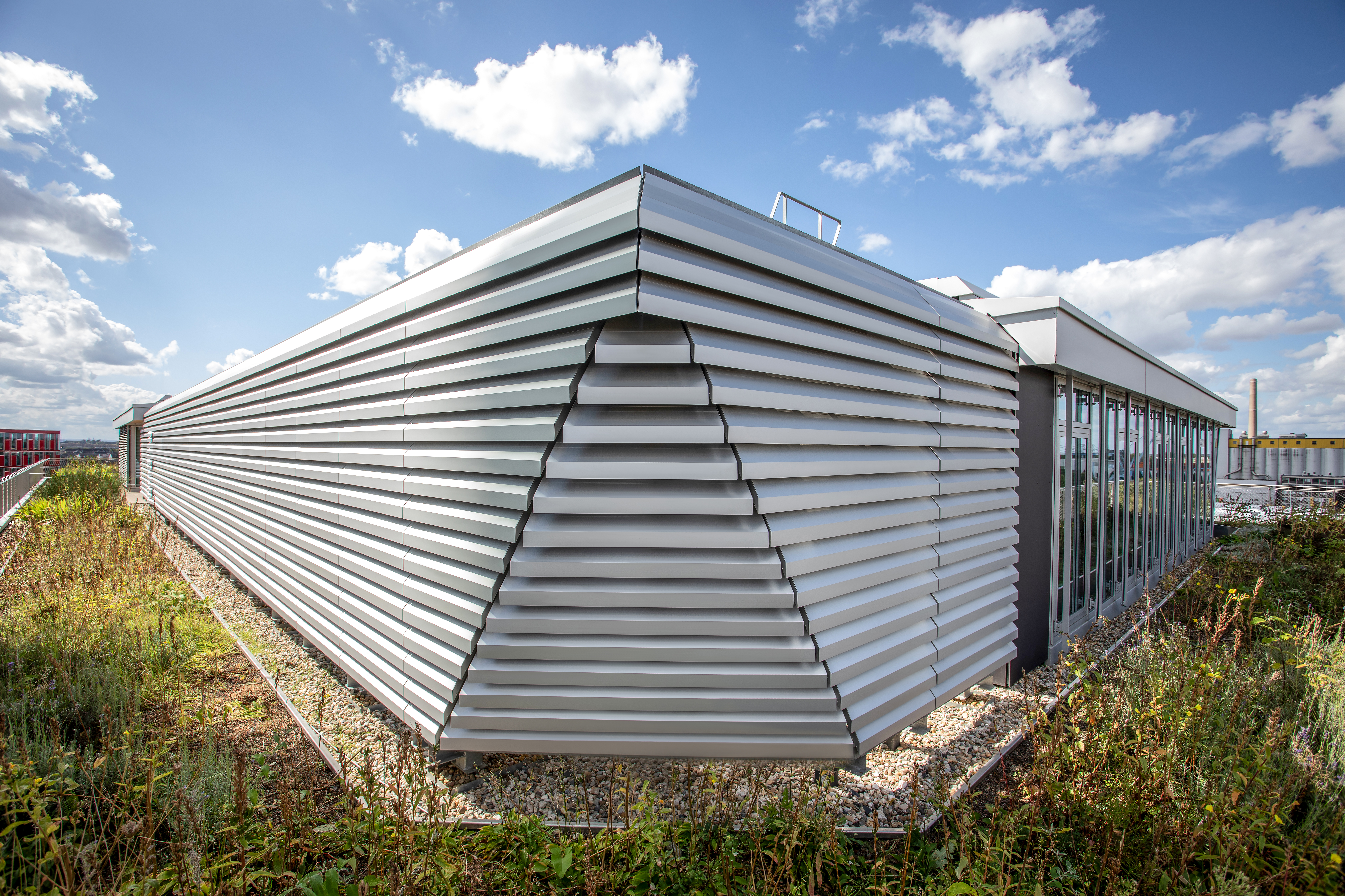 De afgeschuinde lamellenwand op de dakverdieping geeft het gebouw een zekere lichtheid en elegantie. Bron: Renson